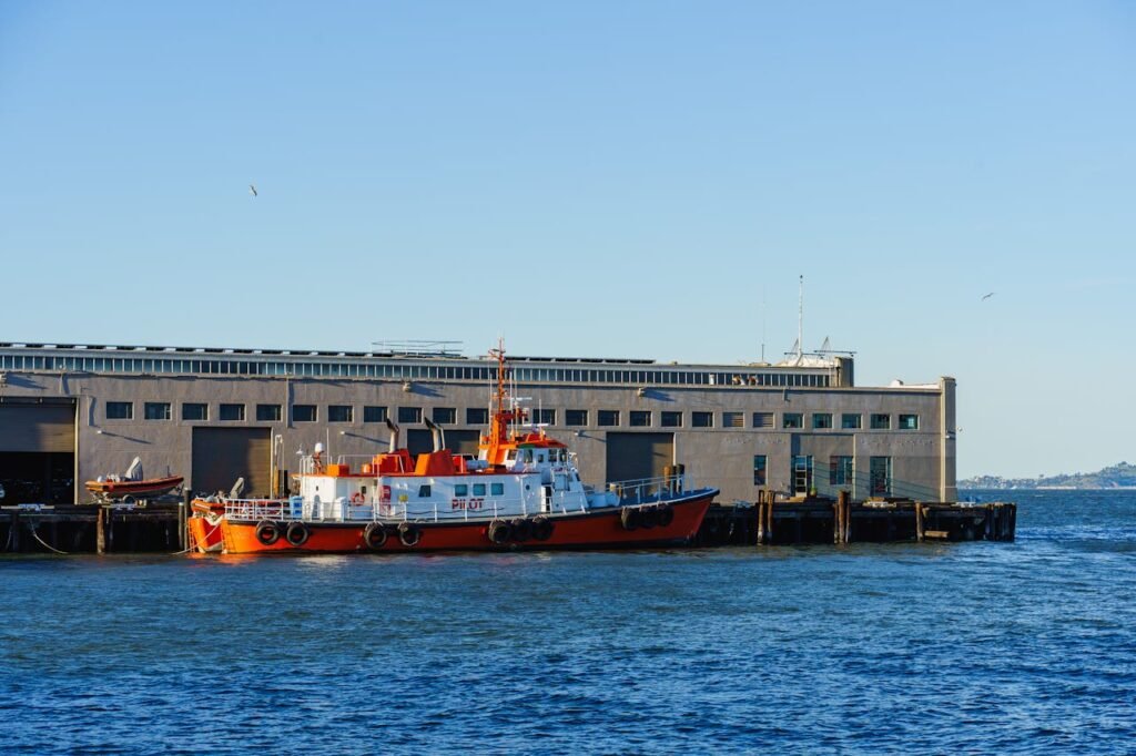 Bright orange pilot boat stationed at city harbor with clear blue sky.